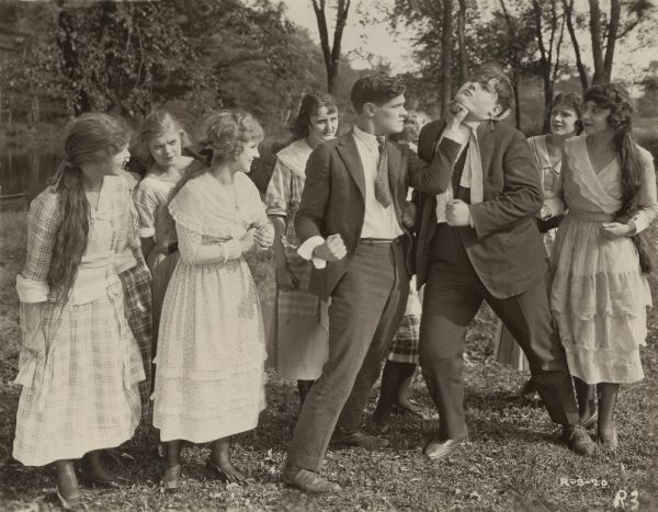 Gilbert Blythe (played by Paul Kelly) punches Jumbo Pie (Lincoln Stedman) on the chin as Anne Shirley (Mary Miles Minter, directly to the left of Paul Kelly) and a group of girls look on.