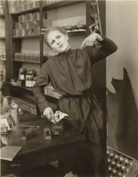 Annie Johnson (played by Mary Miles Minter) is an orphan working in a shop. She has just hit her finger with a hammer while trying to repair a shoe in a scene still for "Annie for Spite."