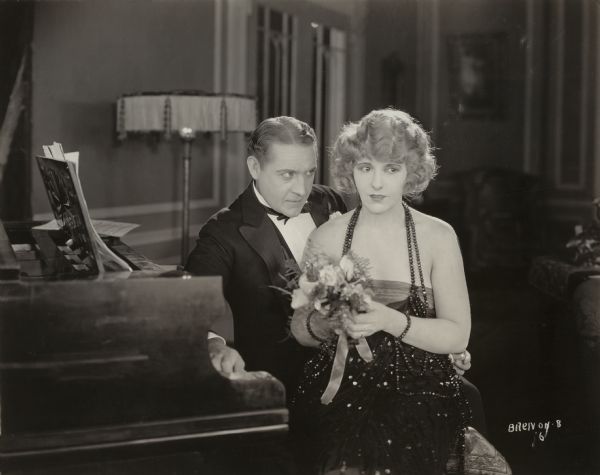 Philip Gray (played by Holmes Herbert) is intent on seducing Myrtle Hill (Pearl White), the wife of his business associate. They sit together, wearing evening clothes, on a piano bench in this scene still for "Any Wife."