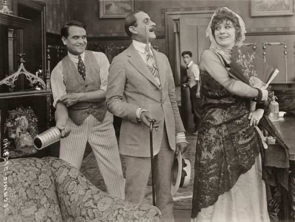 Theodore Crosby (played by a gleeful Franklyn Farnum) prepares to hit Sir Mortimer Beggs (Sam de Grasse) with a liquor bottle. Sir Mortimer is distracted by the flirtatious Señorita Dolores (Claire du Brey). The houseboy Algeron (Frank Tokunaga) is in the background in this scene still from the 1917 Bluebird production "Anything Once."