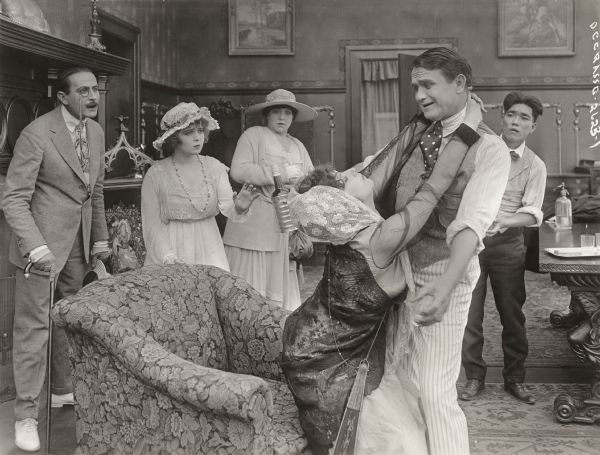 Scene still for the silent film "Anything Once" with, from left to right, Sam de Grasse (playing Sir Mortimer Beggs), Marjory Lawrence (Dorothy Stuart), Mary St. John (Mrs. Stuart), Claire du Brey (SeÃ±orita Dolores), Franklyn Farnum (Theodore Crosby), and Frank Tokunaga (Algeron).