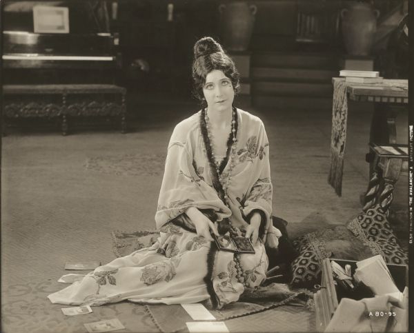 Seated on the carpeted floor, Chichita (played by Elsie Ferguson) models a Japanese-style loose robe trimmed with fur in a publicity still for "The Avalanche." The French fashion house Callot Soeurs provided the costume.