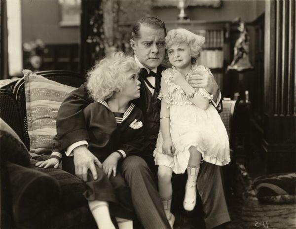 John Hamilton (played by Herschel Mayall) sits on a couch with two children: Roland, who is in a sailor suit, played by Francis Carpenter and Rose, who is crying, (Virginia Lee Corbin). The rubber stamped caption on the reverse of the print reads: "A Gorgeous Picturization of Charms and Adventure for Young and Old, THE BABES IN THE WOODS, Based on the famous old English Ballad. Another Fox exquisite picture made in California, the Grand Canyon of Arizona, and Hawaii."