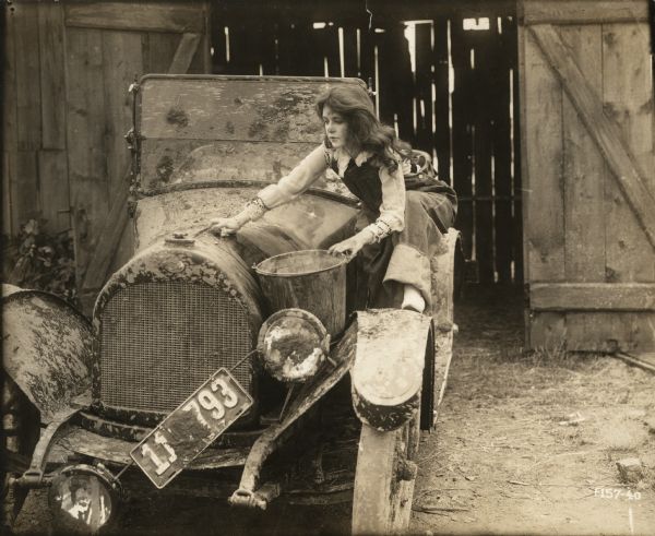Bab Archibald (played by Marguerite Clark) washes a very muddy automobile that appears to be an Overland open touring car in this scene still for "Bab's Burglar."