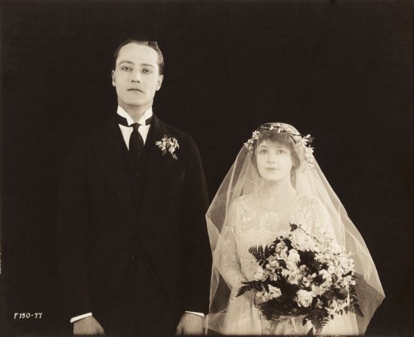 William Hinckley and Marguerite Clark stand side by side costumed for a wedding as groom and bride in a publicity still for the Famous Players production of "Bab's Matinee Idol."