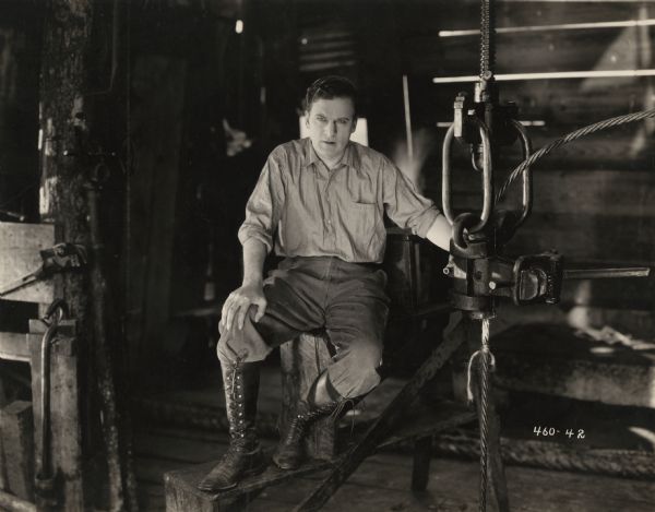 Dressed in the clothes of a roughneck (chambray shirt, corduroy pants, high lace-up boots), Tom Redding (played by Thomas Meighan) works on an oil rig and looks very weary. This is a scene still for the 1922 silent drama "Back Home and Broke."