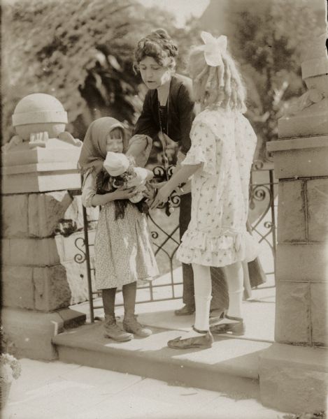 Actress Mae Gaston gives a baby doll to a poor flower girl as an older and more prosperous girl looks on in a scene still from the 1915 Reliance film "The Balance."