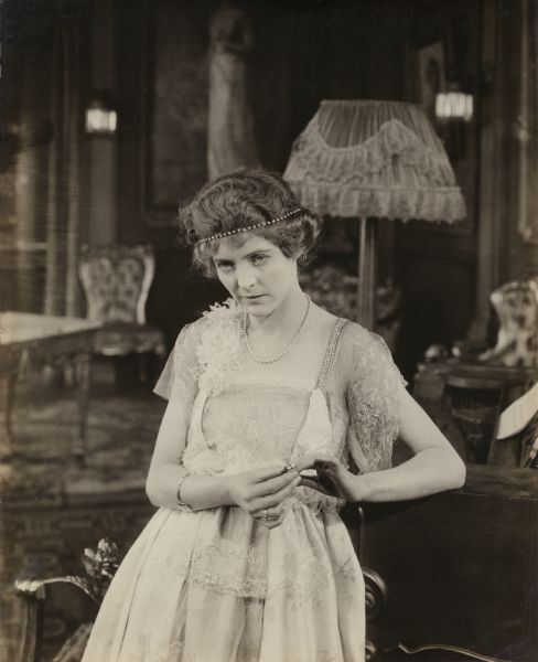 With a cold and calculating look on her face, Hope Merrill, played by Mabel Taliaferro, fondles a engagement or wedding ring on her finger in a scene still for the silent drama "The Barricade."
