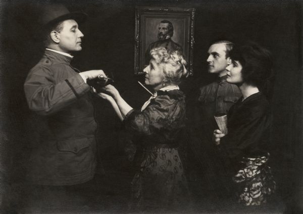 Mrs. Harrison (played by Mary Maurice) solemnly presents the family sword to her son John Harrison (Charles Richman, on the left) in a scene still for the 1915 silent film "The Battle Cry of Peace." Watching are Virginia Vandergriff (played by Norma Talmadge), a Civil War ancestor in a portrait painting, and the younger son Charley Harrison (James Morrison). The brothers wear U.S. Army uniform tunics.
