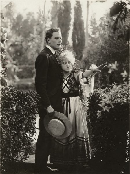The cousins Pepe Rey Don Jose (played by Emory Johnson) and Rosarita (Ella Hall) stand in a Spanish garden looking apprehensive in a scene still from the 1918 Universal drama "Beauty in Chains."