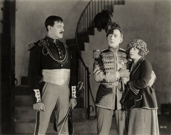 The evil Maldonado (played by Montagu Love) glares at Dr. Arbutus Bud (Raymond Hitchcock in an aristocratic uniform) and his daughter Ann Bud (Diana Allen) in a scene still for the 1922 silent comedy "The Beauty Shop."