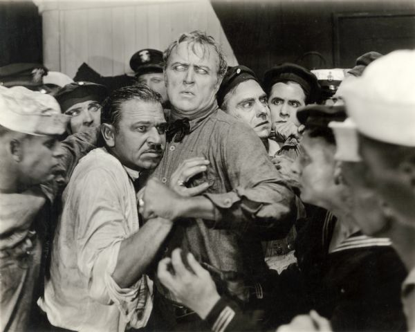 German U-boat commander Lieutenant Brandt (played by Wallace Beery) and American Merchant Marine Captain Oscar Krug (Hobart Bosworth) face a crowd of angry American sailors in a scene still for the silent drama "Behind the Door."