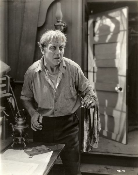 In a scene still for the silent drama "Behind the Door," American Merchant Marine Captain Oscar Krug (played by Hobart Bosworth) holds a straight razor in his bloody hands. For revenge, he has attempted to skin a German submarine commander (played by Wallace Beery) whose shadow is seen in the background.
