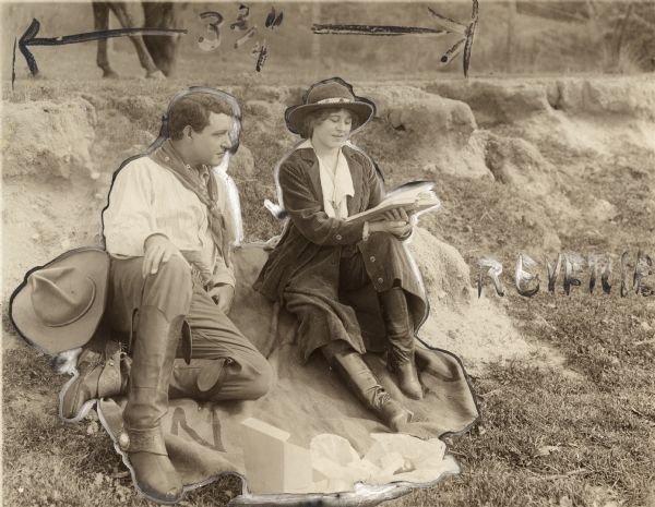 Ben Blair (played by Dustin Farnum in cowboy costume) has a picnic on the ground with Florence Winthrop (Winifred Kingston, wearing a corduroy riding suit). She reads from a book, and a horse grazes in the background in this scene still for the silent drama "Ben Blair" that has been heavily retouched and annotated for publication.