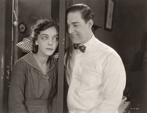 Nancy Scroggs (played by Zasu Pitts) and Peter Van Alstyne (David Butler) flirt in a doorway in a scene still for the silent drama "Better Times."