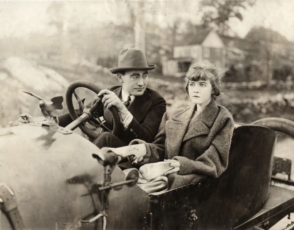Owen Moore is behind the wheel of a two-seat open roadster automobile with Dorothy Gish beside him in this scene still for the silent drama "Betty of Graystone." She looks worried and carries her muddy shoes in her hands.