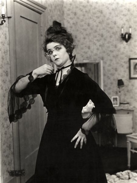 Betty Marshall (played by Olive Thomas) masquerades as an old landlady in this scene still for the silent drama "Betty Takes a Hand." She peers quizzically through a lorgnette.