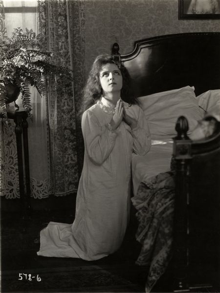 Wearing her nightgown, Betty (played by Olive Thomas) prays beside her bed in a scene still for the silent drama "Betty Takes a Hand."