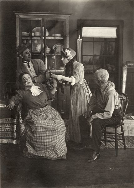 The farmer's wife (played by an unidentified actress) and hired hand (Owen Moore) cower as Betty the cook (Florence Lawrence) threatens to dose the wife with a spoonful of Indian Cure-All patent medicine in a scene still for the silent comedy "Betty's Nightmare." The actor playing the farmer is also unidentified.