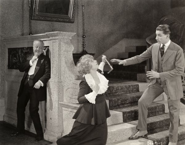 Sally Marrio (played by Pearl White) appears to be falling with a rake end poker in her hand as the banker J. Peter Weathersby (Louis Haines) watches from behind and as another man, probably blackmailer Lester Lawton (played by Arthur Gordini), reaches out toward her in a scene still from silent melodrama "Beyond Price."