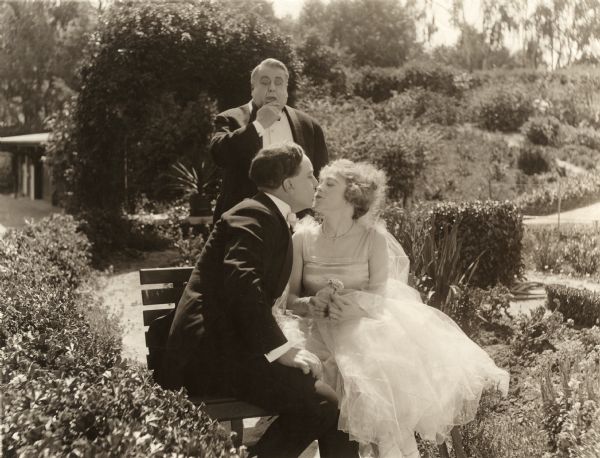 Alice's wealthy benefactor (played by Daniel Gilfether) is surprised to discover Alice (Jackie Saunders) kissing James Morgan (Arthur Shirley) on a garden bench in this scene still for the silent drama "A Bit of Kindling."
