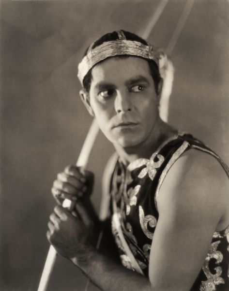 In this dramatically lit publicity still for the silent drama "Look Your Best," Antonio Moreno wears what appears to be an exotic cupid costume with a headband. He holds a bow in his hands. Carlo Bruni, Moreno's character in the film, is a dancer.