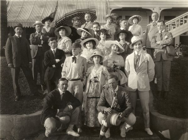 Posed beside the Hotel del Coronado in Coronado, California, are the cast and crew of the 1916 silent drama "Little Eve Edgarton." Crouched in front in striped pants and holding a parasol is the director Robert Z. Leonard. Left of Leonard, with her hand on his shoulder, is the lead actress Ella Hall. Left of Hall, in deerstalker hat and pince-nez is Thomas Jefferson, who played Hall's father, a botanist. Just behind and between Hall and Jefferson is Gretchen Lederer with a white feather boa around her neck. To the right of Lederer is Doris Pawn, and to the right of Pawn, in a white linen suit and Panama hat, is Herbert Rawlinson, the leading man. The actor in the far top right may be Marc Fenton.