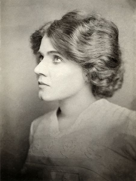 Head and shoulders studio portrait of Florence Lawrence from about the time she joined the Mutoscope and Biograph Company in 1908. She looks up to the left, nearly in profile, and wears a white blouse with embroidered oak leaves.
