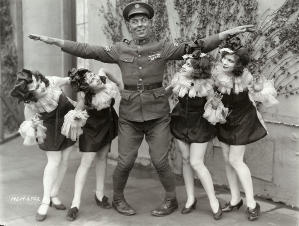 Karl Dane, wearing the U.S. Army sergeant's costume for the 1927 film "Rookies," shows how he towers over four chorus girls in an MGM publicity still.