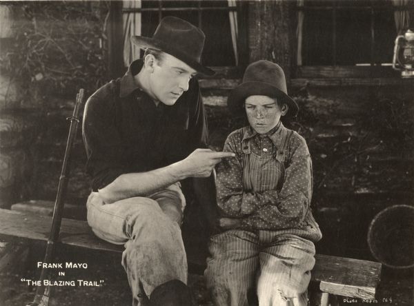 Bradley Yates (played by Frank Mayo) tells Chipmunk Grannis (the child actor Verne Winter) something he does not enjoy hearing in a scene still for the 1921 silent drama "The Blazing Trail." Winters has a face full of freckles and is costumed as a mountain boy in overalls and an adult's worn out hat.