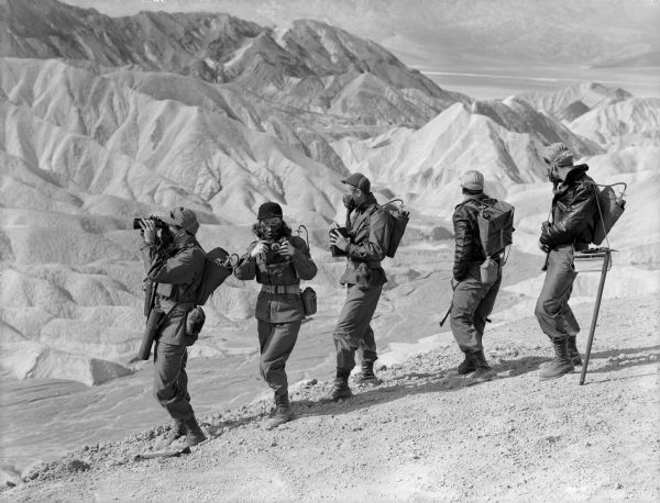 The crew of Rocketship X-M, wearing oxygen masks, surveys the rugged terrain of Mars. From left to right they are played by John Emery, Osa Massen, Lloyd Bridges, Noah Beery Jr., and Hugh O'Brian.