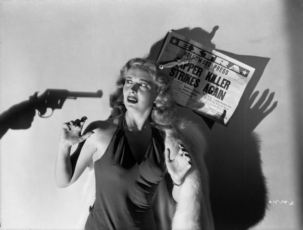 Actress Mary Meade is threatened by the shadow of a revolver in a publicity still for the 1947 Eagle-Lion release "T-Men." Pinned to the wall behind her by a dagger is a newspaper with the headline "Stripper Killer Strikes Again."
