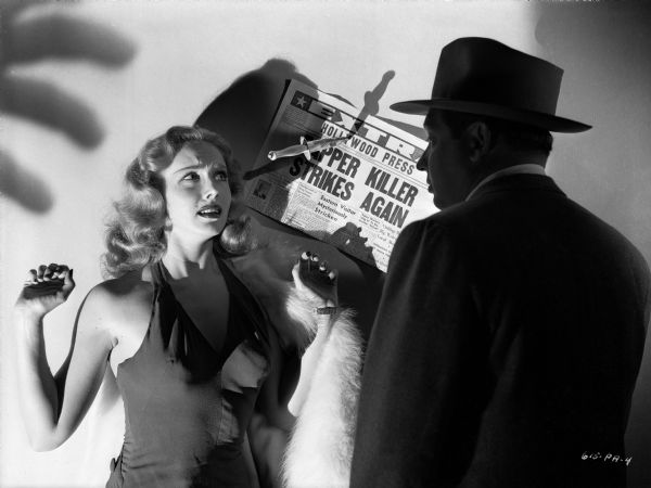 Actress Mary Meade is menaced by a man in silhouette, possibly Paul Fierro, in a publicity still for the 1947 Eagle-Lion release "T-Men." The shadow of grasping fingers hovers above her head and a dagger pins to the wall a newspaper with the headline "Stripper Killer Strikes Again."