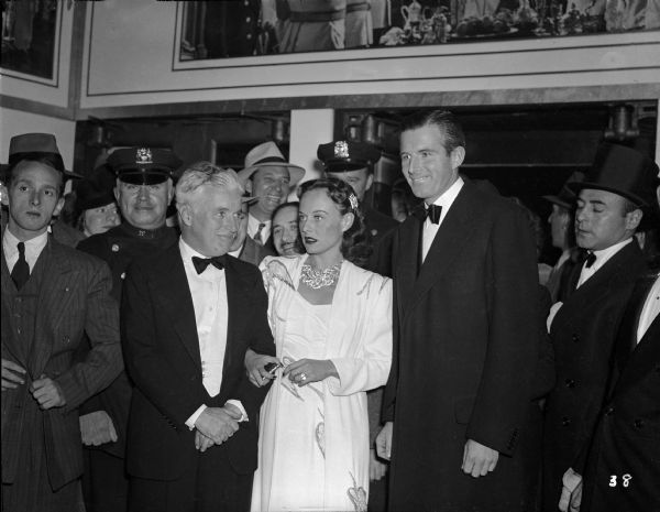 Charlie Chaplin, Paulette Goddard, and Tim Durant pose for the photographers in the crowded lobby of the Capitol Theatre during the premiere of "The Great Dictator" on October 15, 1940.