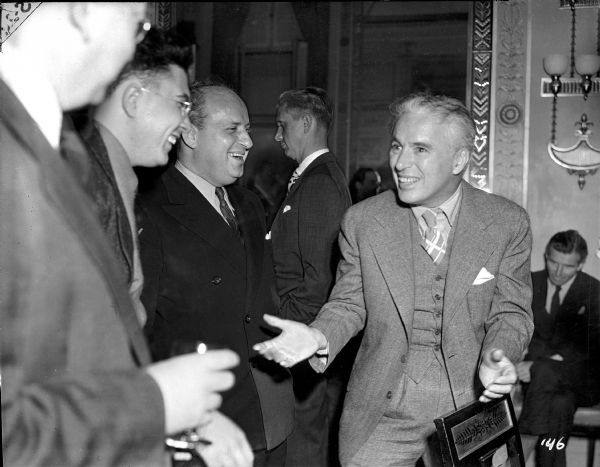 Charlie Chaplin entertains the press at a press conference held at the Waldorf-Astoria in New York on October 13, 1940, to promote "The Great Dictator." United Artists executive Maurice Silverstone, balding and in a dark suit, stands beside Chaplin on the left.