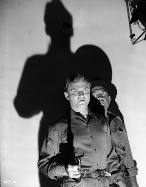 Don "Red" Barry with pistol drawn and Frank Richards in his shadow pose in a dramatically lit publicity still for "Tough Assignment."
