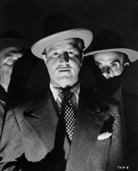 Dramatically lit publicity still with three gangsters, from left to right Frank Richards, an unidentified actor, and Marc Lawrence, for the 1949 production "Tough Assignment."
