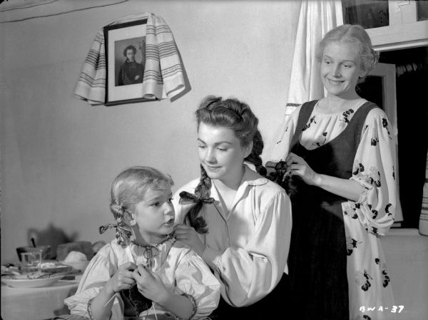 The women of the Ukrainian Pavlov family braid hair in a publicity still for "The North Star." From left to right the actresses are Ann Carter, Anne Baxter, and Ann Harding.