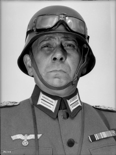 Erich von Stroheim poses full-face in his costume as the German military doctor Otto von Harden in a publicity still for "The North Star." He wears a steel helmet (Stahlhelm) on which are a pair of goggles.
