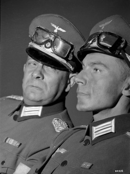 Erich von Stroheim (left) looks warily at Martin Kosleckin in a publicity still for "The North Star." They are costumed as the German military doctors von Harden and Richter. Both wear officers' visor caps on their heads with goggles stored above the visors.