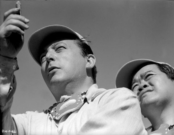 Director Lewis Milestone uses a cigar to line up a shot with his cinematographer James Wong Howe looking over his shoulder in a production still for "The North Star."