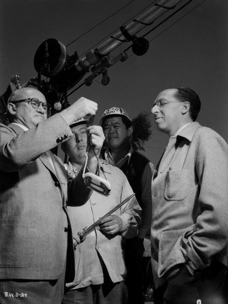 In an outdoor production still for "The North Star," producer Samuel Goldwyn (left) examines a short strip of 35mm film while director Lewis Milestone, cinematographer James Wong Howe, and composer Aaron Copeland look on.