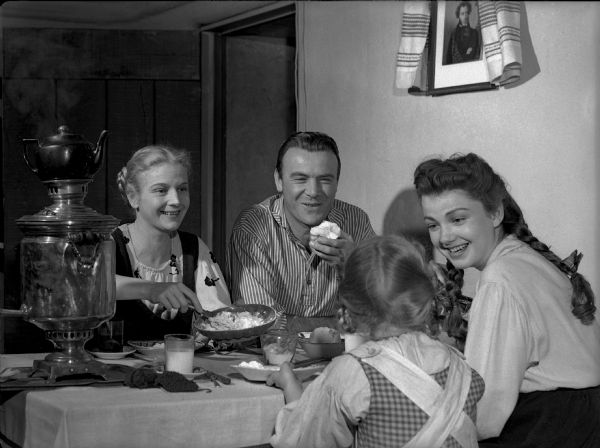 The Pavlov family sits happily around the supper table in a publicity still for "The North Star." From the left, the actors are Ann Harding, Dean Jagger, Ann Carter (back only), and Anne Baxter.