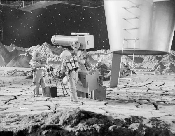 Two astronauts in spacesuits unload equipment from their spaceship onto the surface of the moon. One has camera equipment including an 8mm Bolex motion picture camera on a tripod. The other carries a large telescope with ease due to the lack of strong gravity.