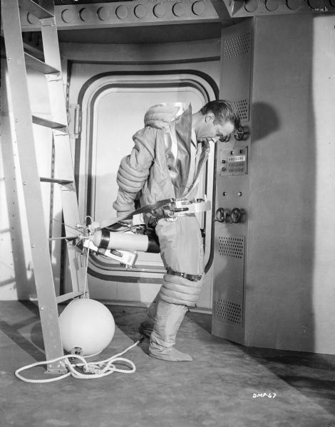 Actor Warner Anderson struggles with his spacesuit in a spaceship's airlock in a scene still for "Destination Moon."