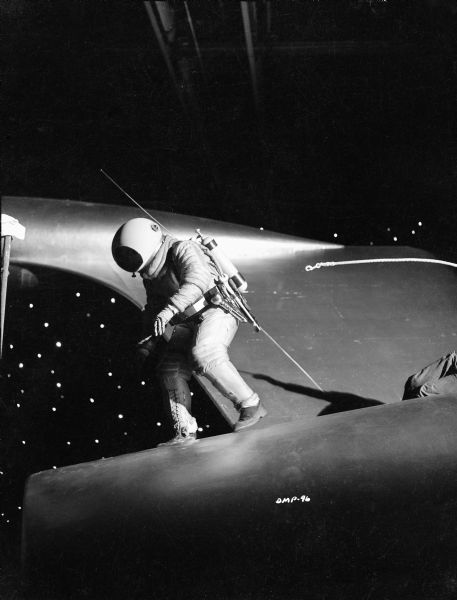 An astronaut walking on the hull of a spaceship has become untethered from his safety line. The knees of the technician operating the prop safety line can be seen on the right.