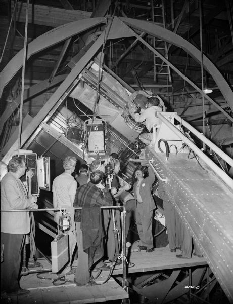 Technicians for the 1950 science fiction film "Destination Moon" look into the rotatable set of a spaceship interior. A rotatable Technicolor motion picture camera is mounted on a crane.