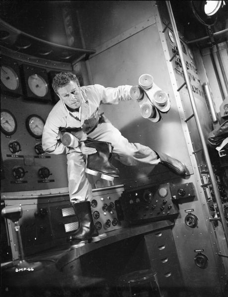 With one foot on a desk and the other on a wall, actor John Archer simulates weightlessness in a scene still for "Destination Moon." He wears suction boots and carries two more pairs.