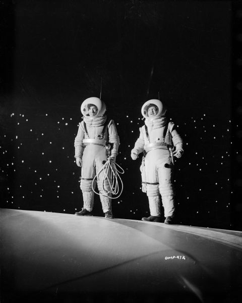 Two astronauts, played by Dick Wesson (left, holding rope) and Tom Powers, stand on the hull of their spaceship and watch in dismay as an offscreen companion floats away into space.