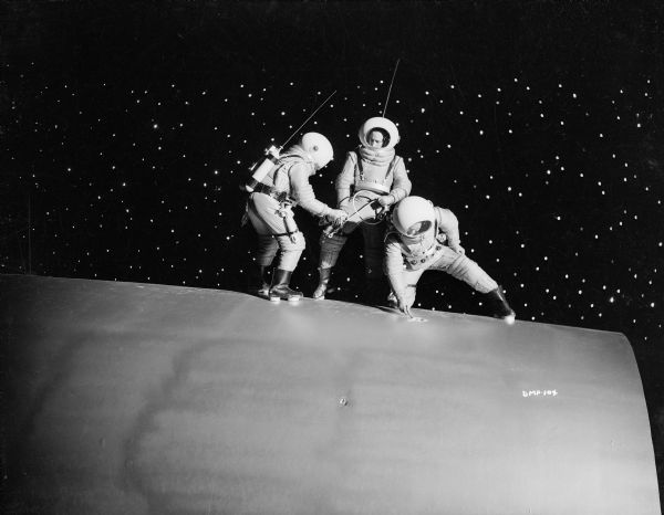 Three astronauts standing on the exterior of their spaceship prepare to attach a safety line to the hull in a scene still for "Destination Moon."